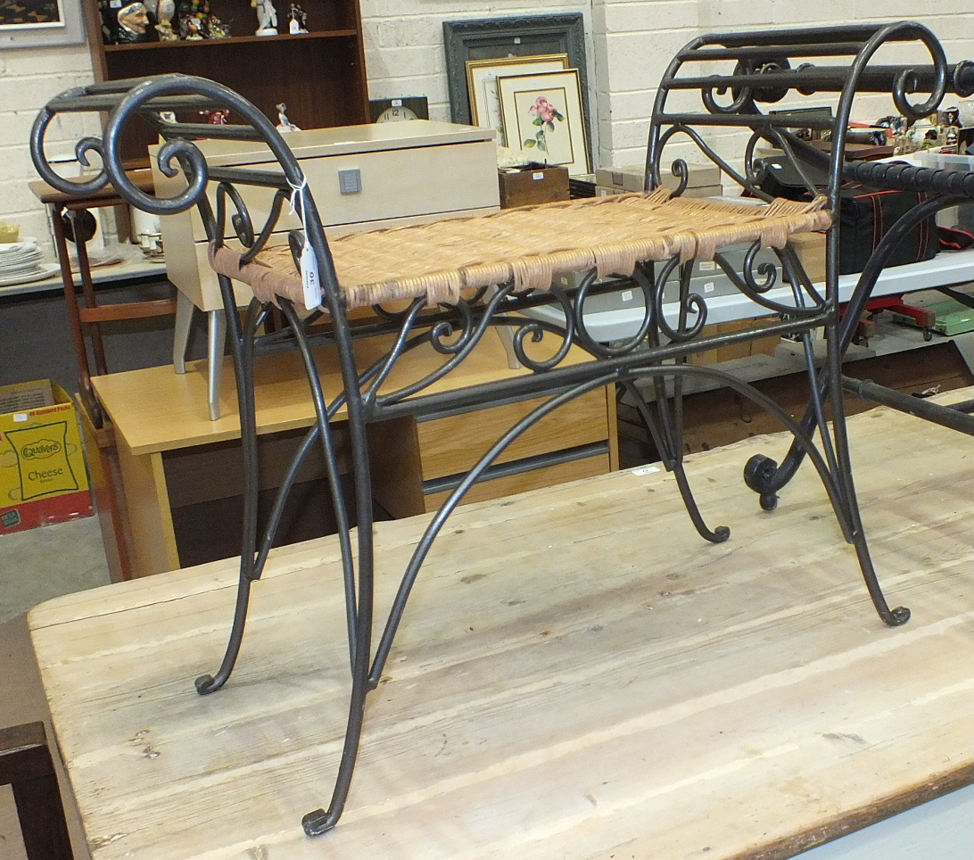 A 20th century wrought metal scroll-work stool with caned seat, 77cm long, 59cm high.