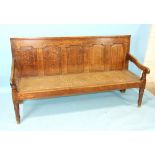 An antique oak settle with fielded panelled back and plain slab arms, on turned front legs, 183cm