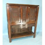 An antique oak side cupboard having a pair of Gothic carved doors and central panel above three