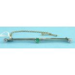 A bar brooch centrally claw set a round-cut emerald with an old brilliant-cut diamond to each end,