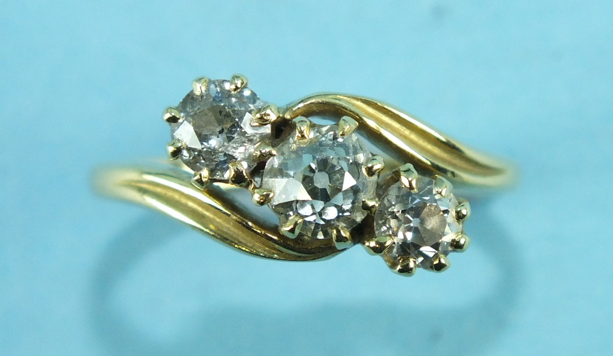 A three-stone diamond cross-over ring, the old brilliant-cut diamonds claw set in 18ct yellow gold