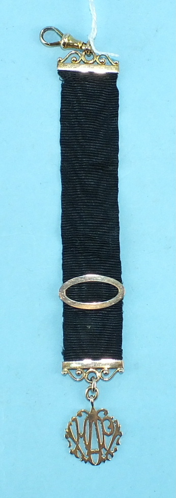 An unmarked yellow metal stylised monogram on yellow-metal-mounted black silk ribbon.