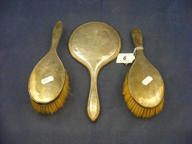 Two silver brushes together with a silver hand mirror