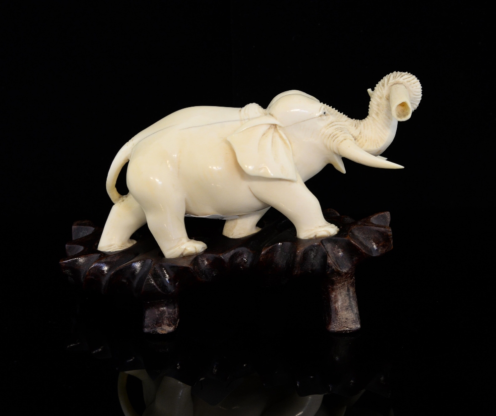 Japanese carved ivory elephant in a walking pose, with a tusk in it's trunk, on hardwood base,