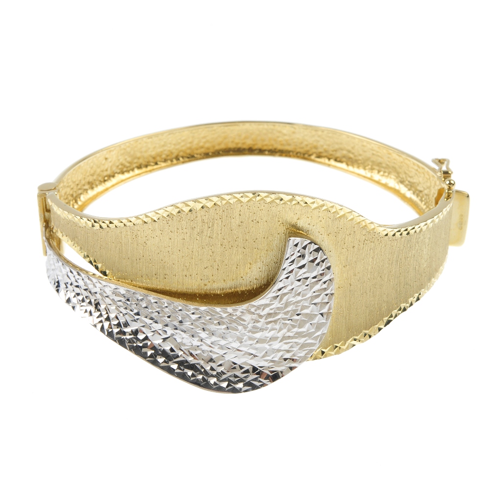 A 9ct gold bi-colour hinged bangle. The textured curved panels, to the tapered half-bangle.
