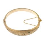 A 1960s 9ct gold emerald and diamond bangle. The textured and tapered half-bangle, with scattered