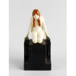 A Royal Worcester figure, modelled as a young naked female with braided hair, kneeling upon brake-
