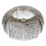 A large hinged bangle. Of hollow design with a main panel tapering to embossed sides, with scrolling