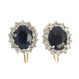 A pair of sapphire and diamond cluster earrings. Each designed as an oval-shape sapphire, within a