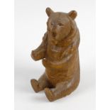 A late 19th century black forest carved wooden bear, in seated pose, the head hinged and opening