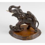 A Japanese Meiji period bronze figure group, depicting an elephant against two tigers, upon a carved