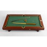 A late 19th century Nuku miniature billiards table. The mahogany frame with beige covered slate,