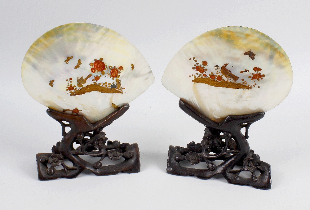 Two late 19th century mother-of-pearl shells, gilt painted with peacocks, each raised upon carved