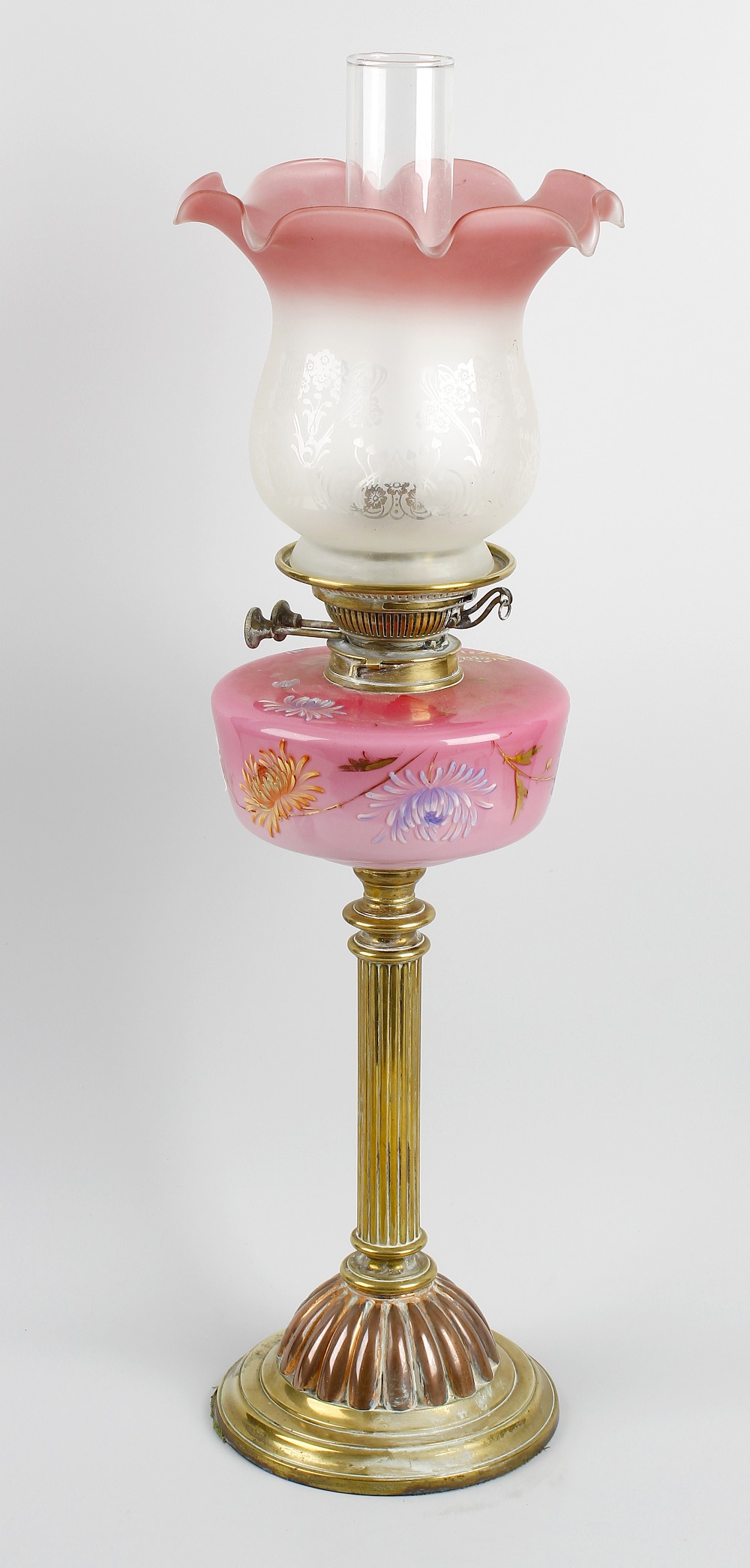 A brass paraffin lamp. The flaring glass shade having frilled rim fading from pink to opaque, raised