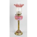 A brass paraffin lamp. The flaring glass shade having frilled rim fading from pink to opaque, raised