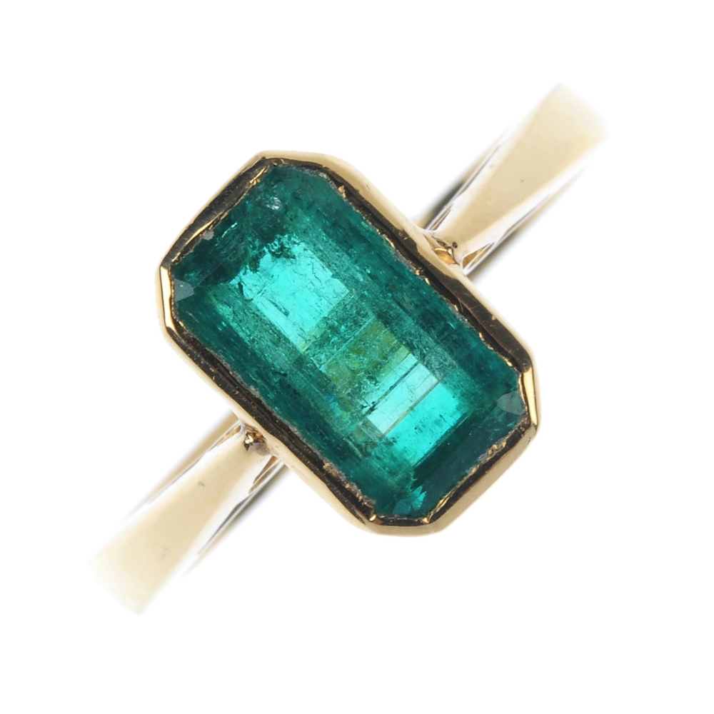 An 18ct gold emerald single-stone ring. The rectangular-shape emerald collet, to the tapered