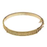 A late 19th century gold hinged bangle. The beaded motif, to the rope-twist border and scrolling