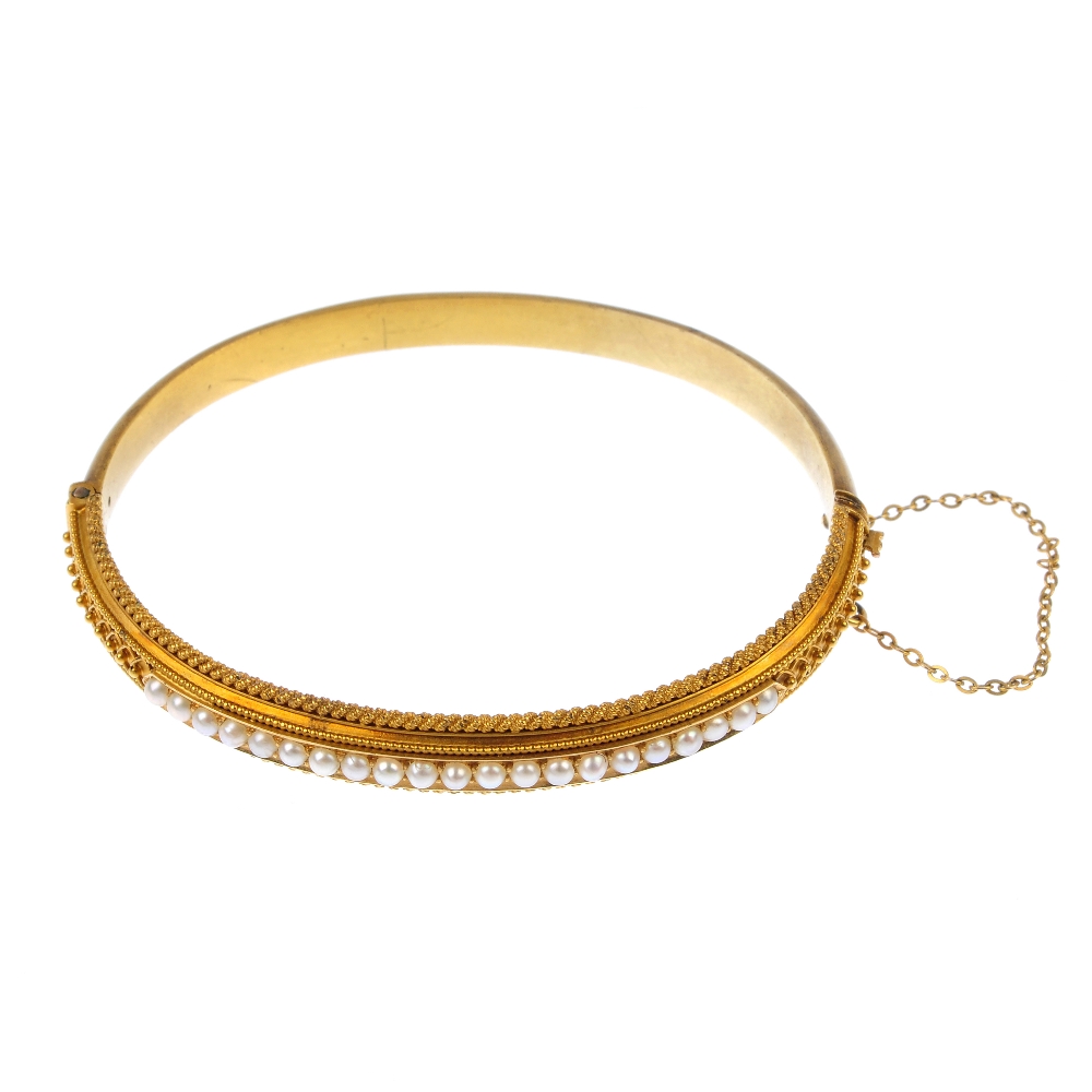 A late 19th century gold split pearl hinged bangle. The split pearl line, to the bead accent sides