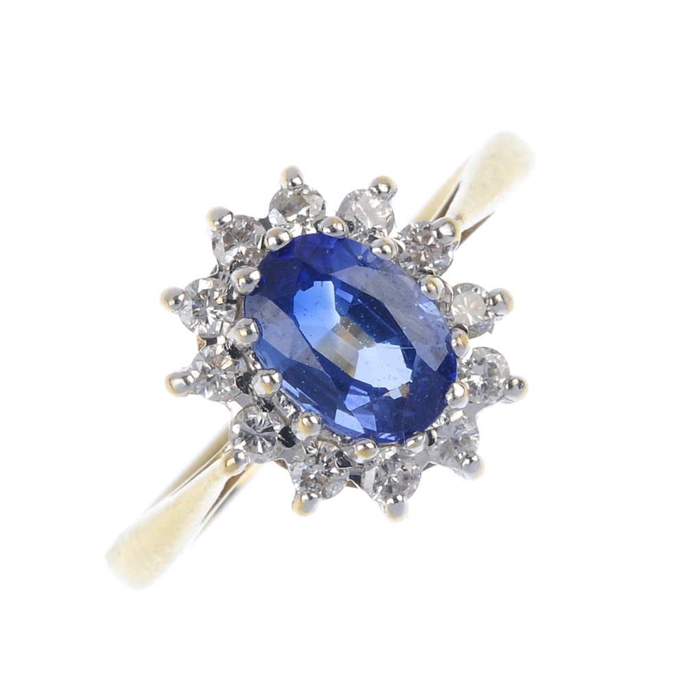 An 18ct gold sapphire and diamond cluster ring. The oval-shape sapphire, within a brilliant-cut