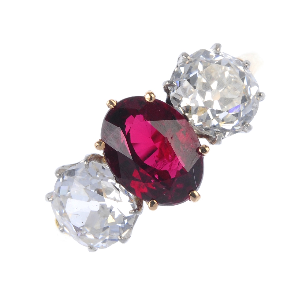 A diamond and ruby three-stone ring. The oval-shape ruby, with old-cut diamond sides, to the plain