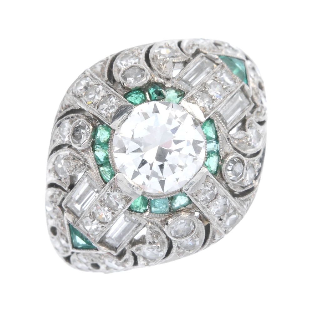 A diamond and emerald dress ring. Of geometric design, the circular-cut diamond, within a calibre-