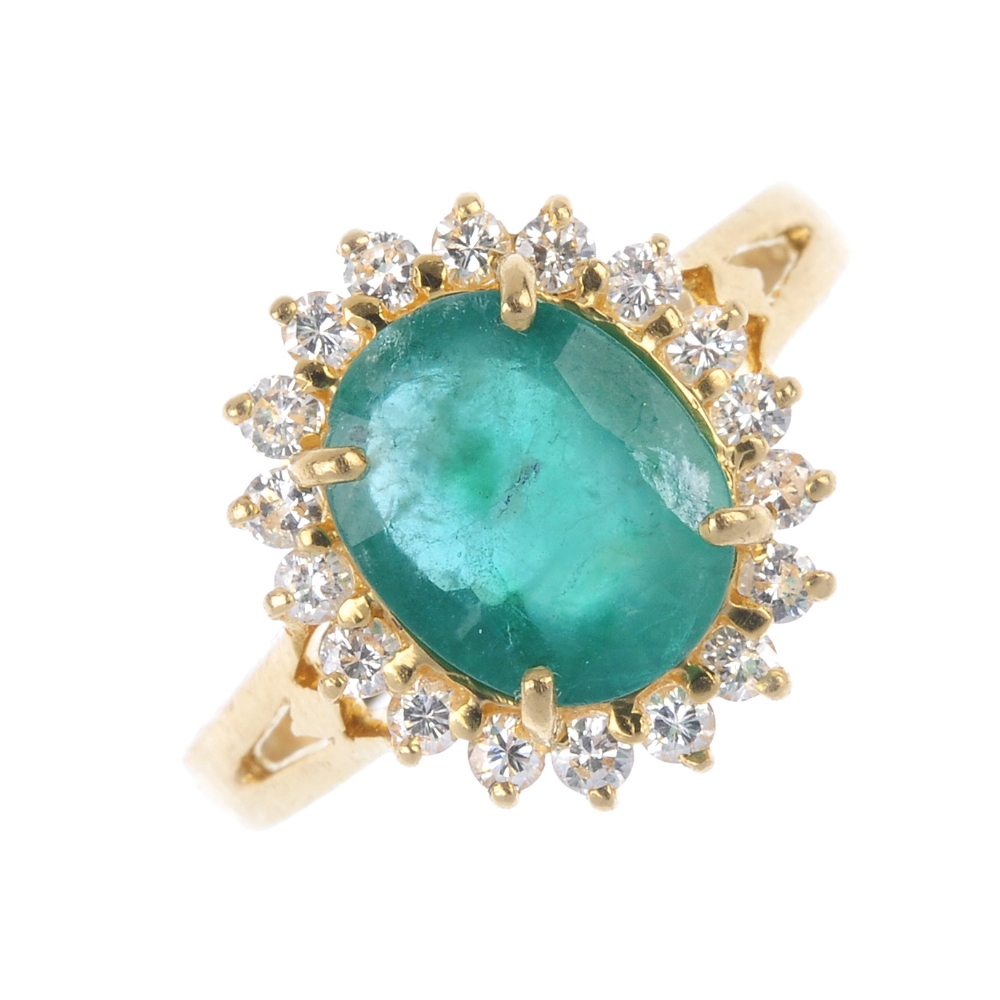 An emerald and diamond cluster ring. The oval-shape emerald, within a brilliant-cut diamond