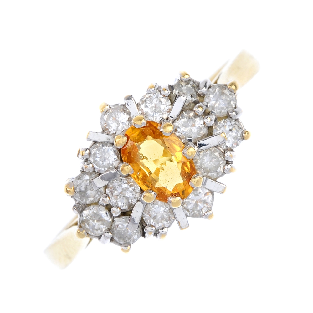 An 18ct gold sapphire and diamond cluster ring. The oval-shape orange sapphire, within an