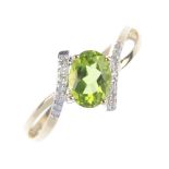 A 9ct gold peridot and diamond crossover ring. The oval-shape peridot, to the single-cut diamond