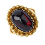 A garnet single-stone ring. The oval garnet cabochon, within a beaded surround, to the bifurcated