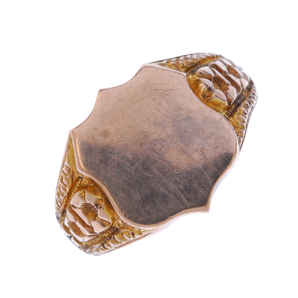 An early 20th century 9ct gold signet ring. The shield-shape panel, to the floral sides and plain