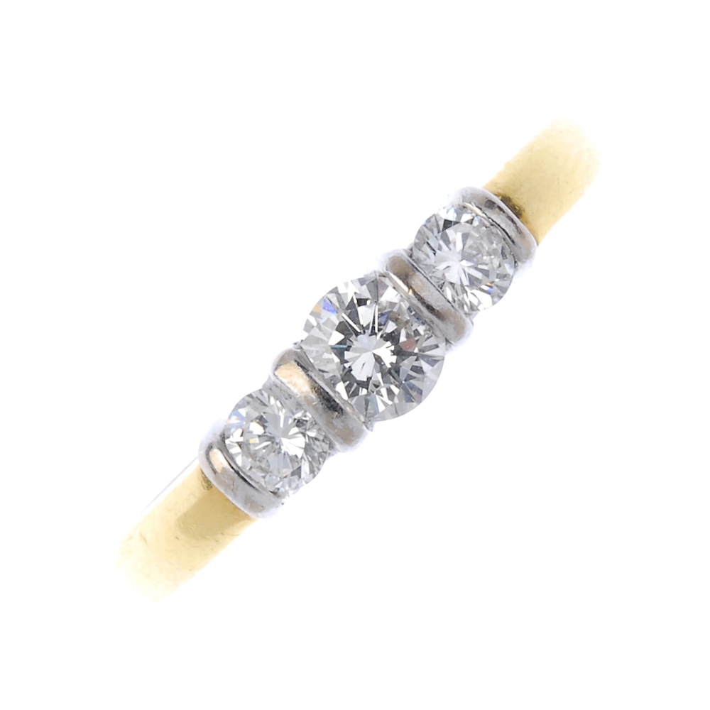 An 18ct gold diamond three-stone ring. The slightly graduated brilliant-cut diamond line, with bar