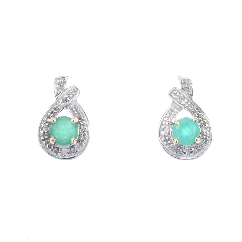 A pair of emerald and diamond earrings. Each designed as a circular-shape emerald, within an
