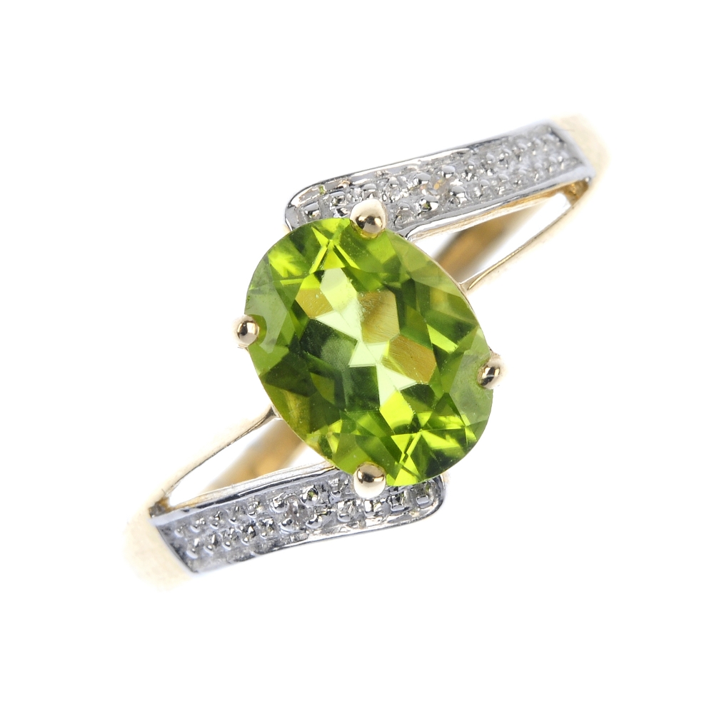 A 9ct gold peridot and diamond crossover ring. The oval-shape peridot, to the single-cut diamond