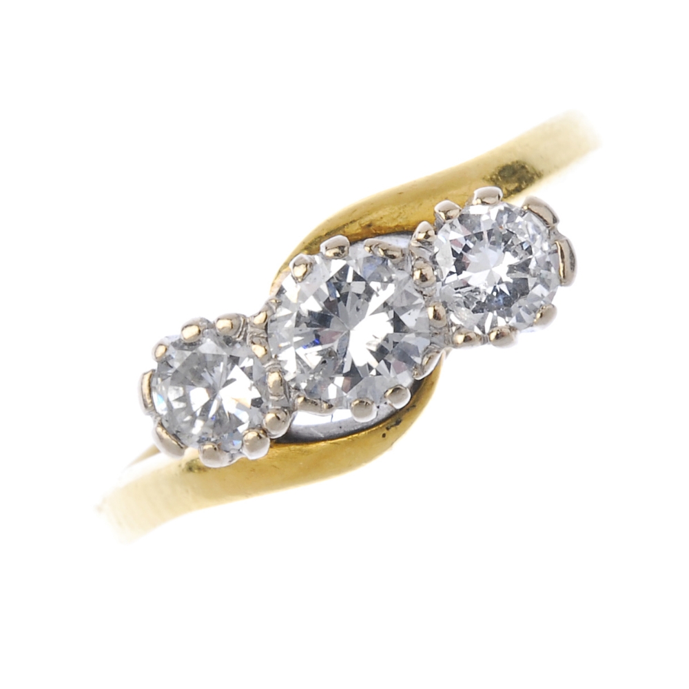 An 18ct gold diamond three-stone ring. The slightly graduated brilliant-cut diamond diagonal line,