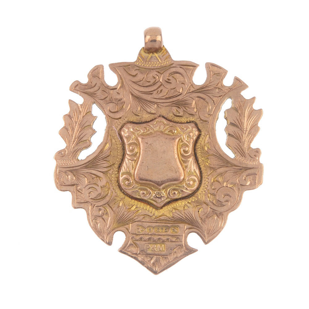 An early 20th century 9ct gold medallion. The raised shield-shape centre, within a scrolling