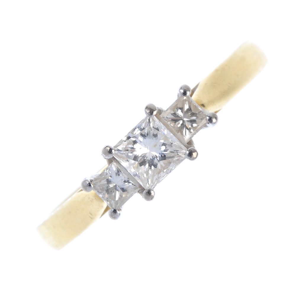 An 18ct gold diamond three-stone ring. The graduated square-shape diamond line, to the tapered