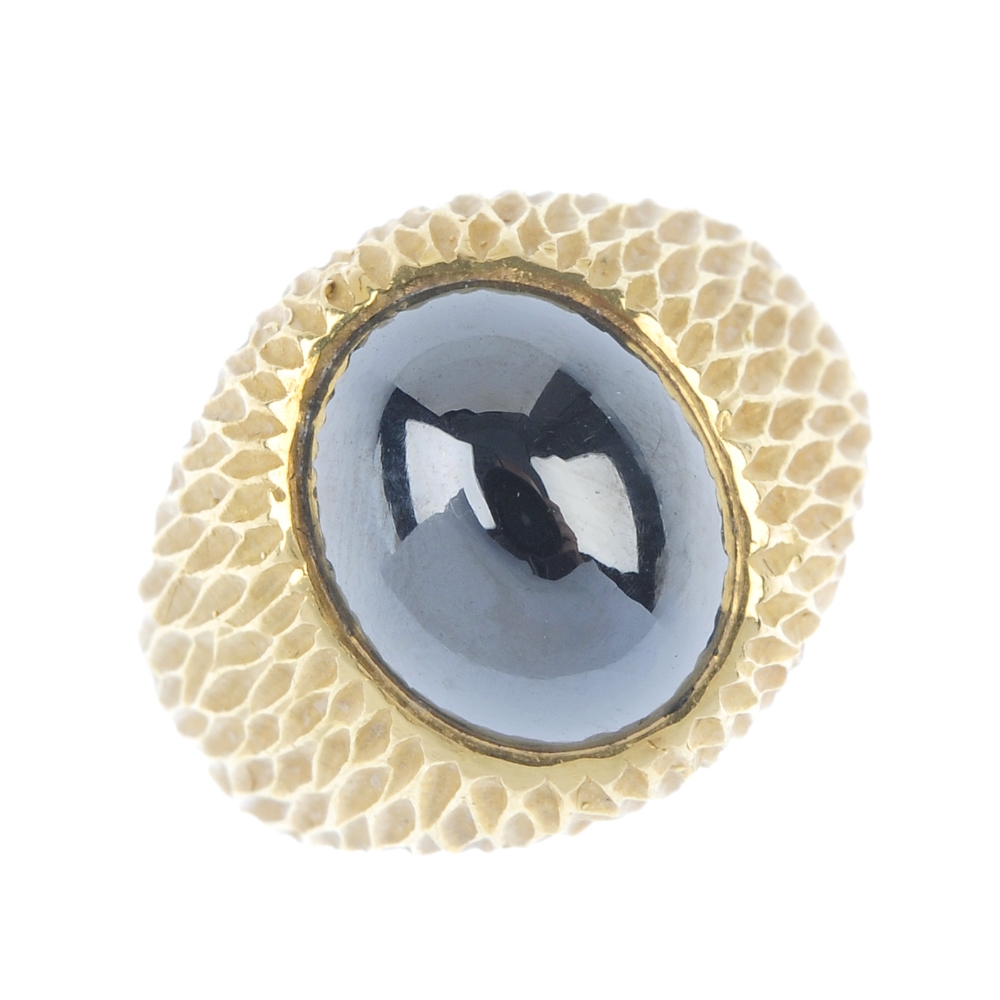 A hematite ring. The oval hematite cabochon, inset to the textured surround and plain half-band.