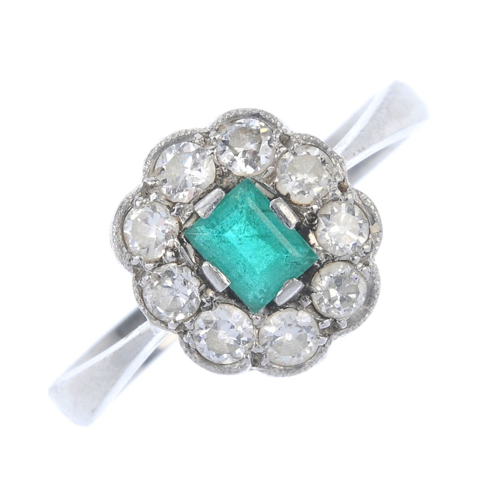 A mid 20th century platinum emerald and diamond cluster ring. The rectangular-shape emerald,