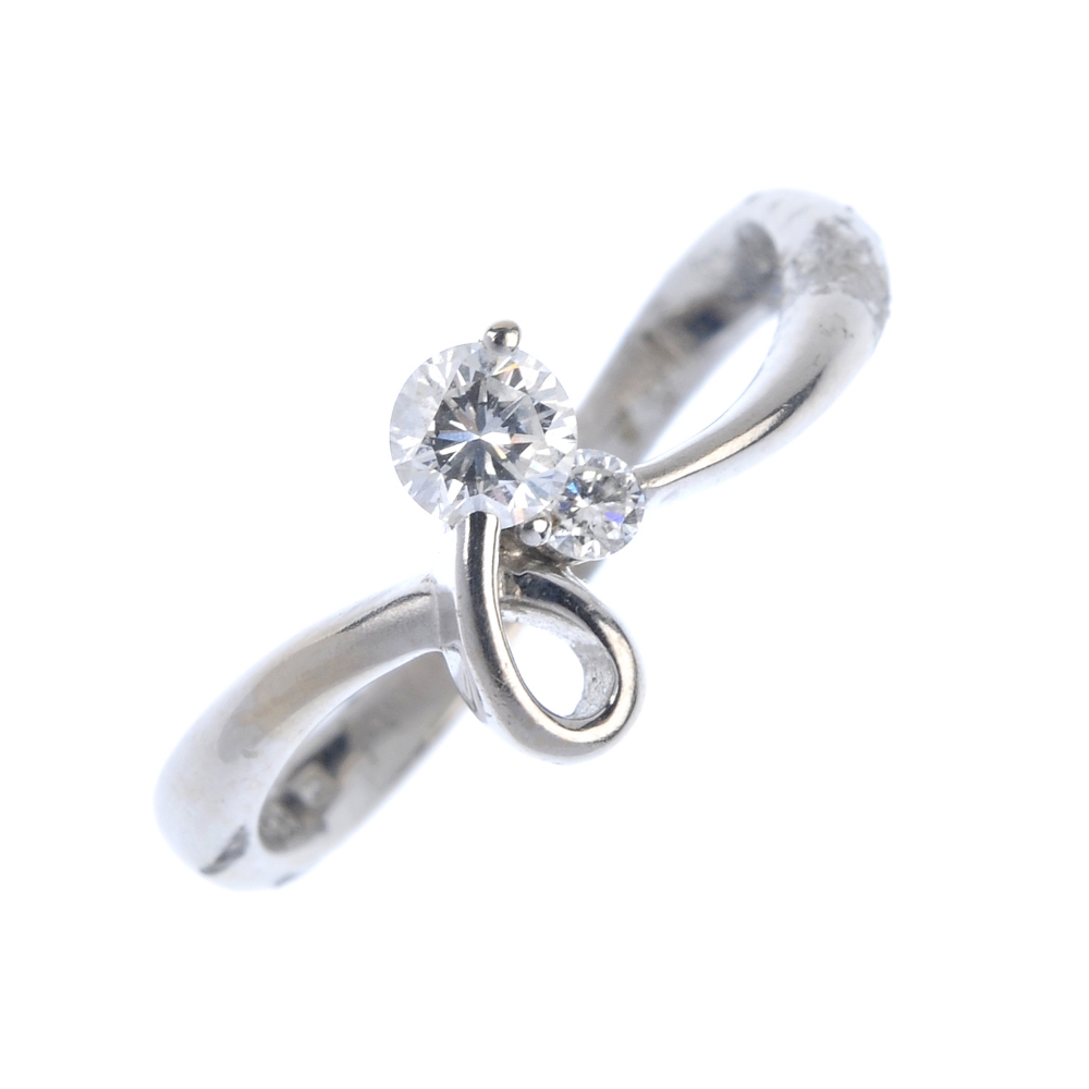 An 18ct gold diamond two-stone ring. Designed as a stylised bow with brilliant-cut diamond