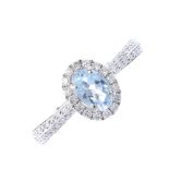 An aquamarine and diamond dress ring. The oval-shape aquamarine, within a brilliant-cut diamond