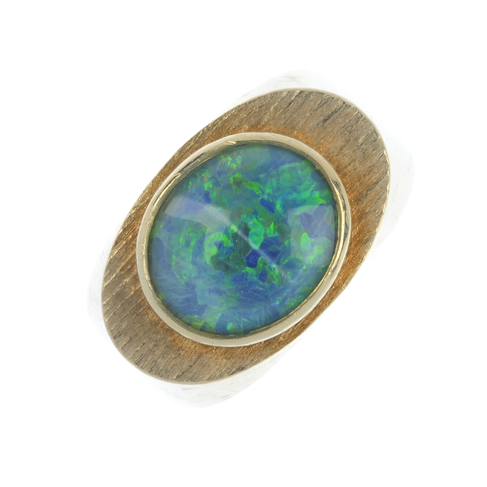 An opal triplet ring. The oval opal triplet, within a textured surround, to the tapered shoulders.