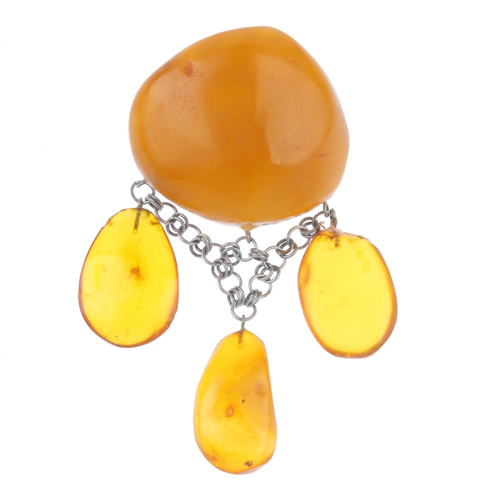 A natural amber brooch. The irregular-shape translucent polished amber panel, suspending three