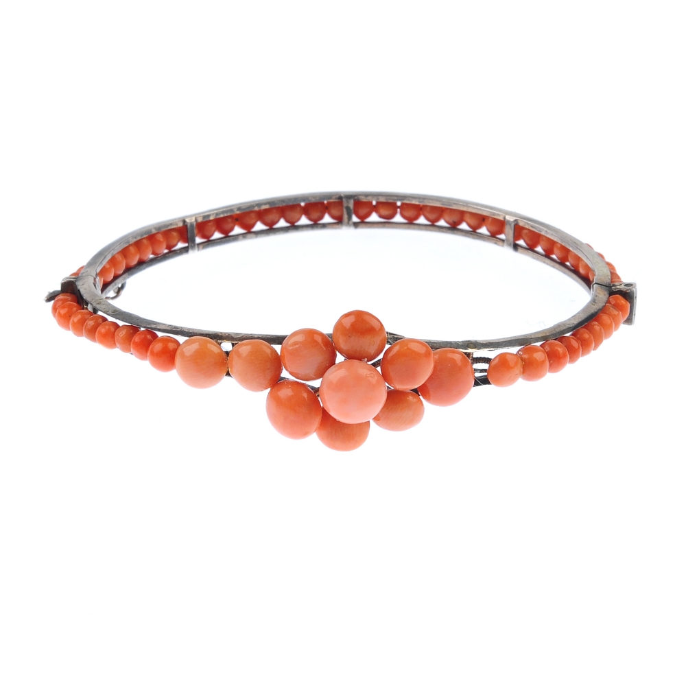 A coral bangle. Designed as a tapered front half bangle set with circular coral cabochons to the