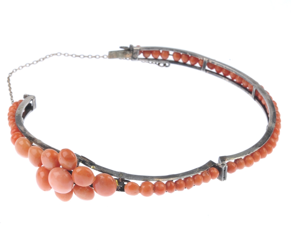 A coral bangle. Designed as a tapered front half bangle set with circular coral cabochons to the - Image 2 of 4
