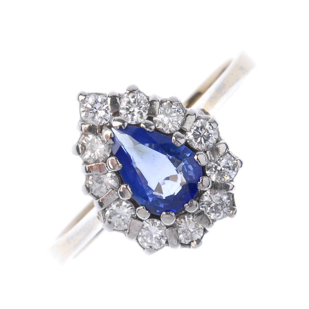 An 18ct gold sapphire diamond cluster ring. The pear-shape sapphire, within a brilliant-cut