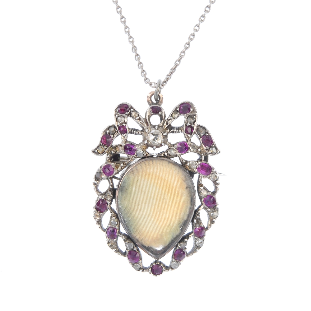 A ruby and diamond photograph pendant. Designed as a vacant pear-shape glazed panel, within a vari-