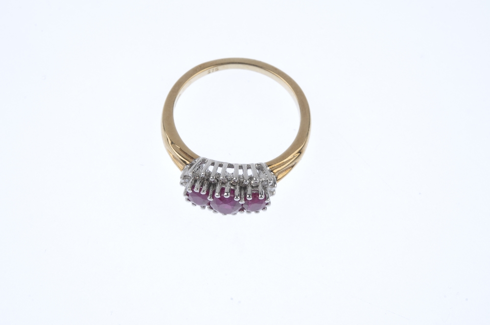 A 9ct gold ruby three-stone and diamond cluster ring. The slightly graduated oval-shape ruby line, - Image 2 of 4