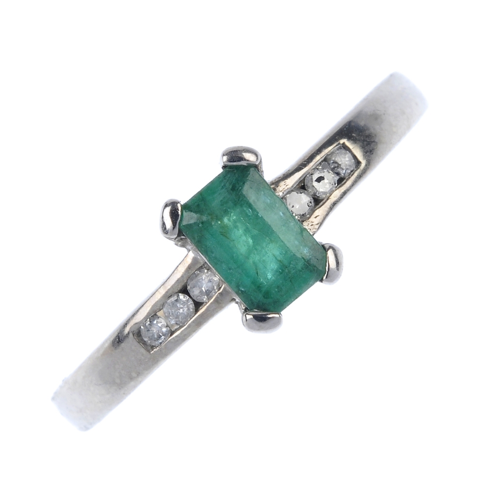 An 18ct gold emerald and diamond dress ring. The rectangular-shape emerald, to the single-cut