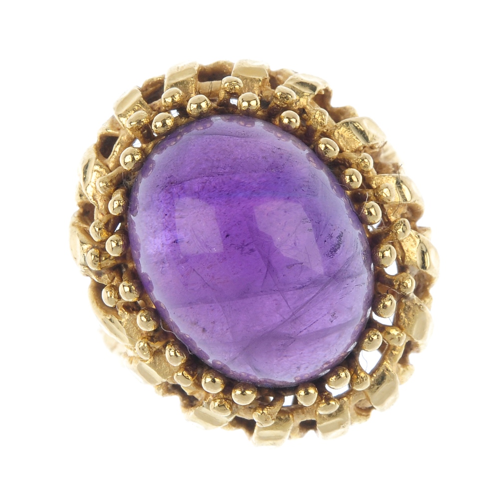 An amethyst single-stone ring. The oval amethyst cabochon, within a bead surround, to the openwork