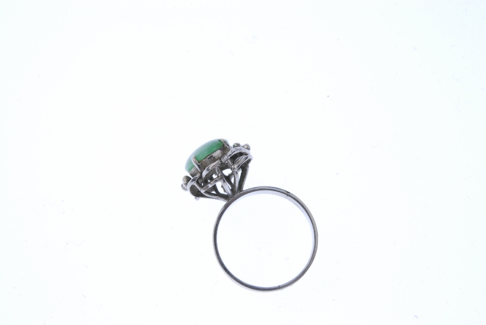 A jadeite dress ring. The oval jadeite cabochon, within a foliate surround, to the plain band. - Image 3 of 4